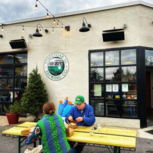 Two patrons wearing winter coats sit at a yellow picnic table outside Streetcar 82 Brewing, a deaf-owned brewery in Washington D.C.