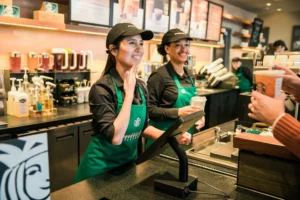 Two dark-haired baristas, both women, use American Sign Language with a customer at Signing Starbucks in Washington D.C.
