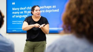 Sarah Honigfeld, a Caucasian woman with dark hair wearing a black top and olive dress pants, signs to a group of administrators during Administrator Summer Immersion Experience.