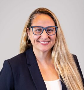 Stacy Abrams, a white woman with glasses and blonde hair wearing a navy blazer over a white shirt poses for her staff photo. Abrams serves as a Project Manager, Early Intervention