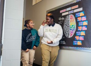 Two Model Secondary School for the Deaf (MSSD) students sign to each other in the hallway.