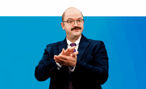 Stephen Farias, Superintendent, Model Secondary School for the Deaf and Kendall Demonstration, Elementary School, dressed in a navy blazer with a magenta tie, signs into camera about Model Secondary School for the Deaf and Kendall Demonstration Elementary School.