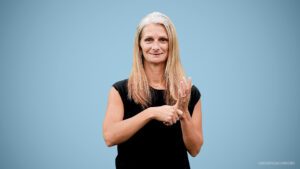 A Caucasian woman with long blonde hair and a black top signs into camera about deaf education resources.
