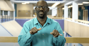 A black man in a green shirt signs to the audience about American Sign Language Standards